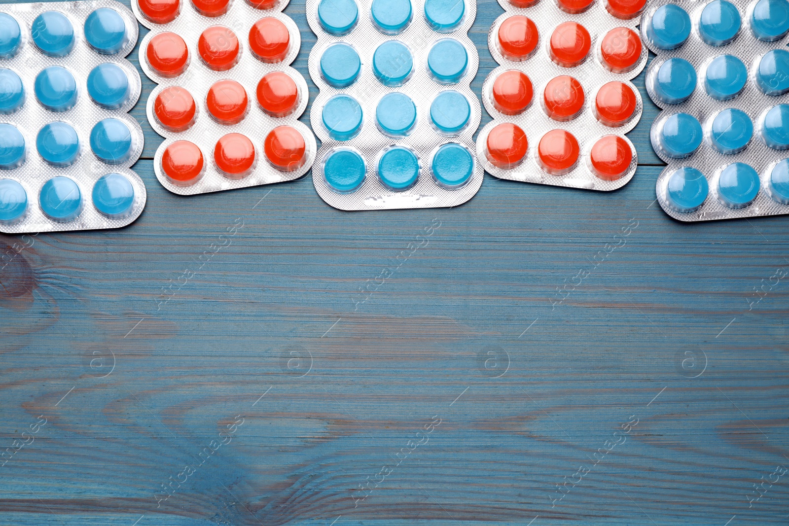 Photo of Blisters with colorful cough drops on blue wooden background, flat lay. Space for text