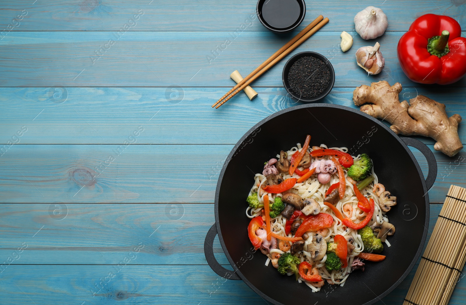Photo of Stir fried noodles with mushrooms, seafood and vegetables in wok on light blue wooden table, flat lay. Space for text