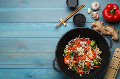Stir fried noodles with mushrooms, seafood and vegetables in wok on light blue wooden table, flat lay. Space for text