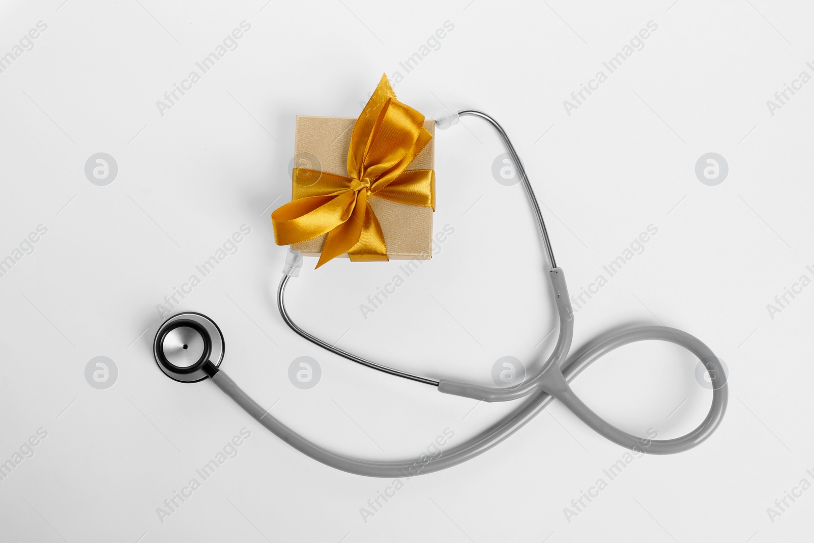 Photo of Stethoscope and gift box on white background, flat lay. Happy Doctor's Day