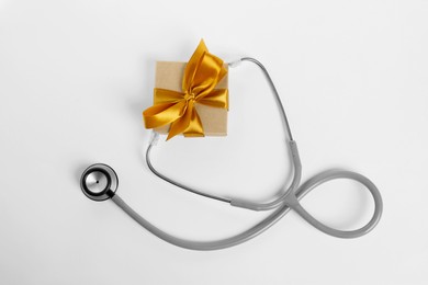 Photo of Stethoscope and gift box on white background, flat lay. Happy Doctor's Day