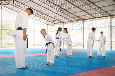 Photo of Children and coach in kimono performing ritual bow before karate practice on tatami outdoors