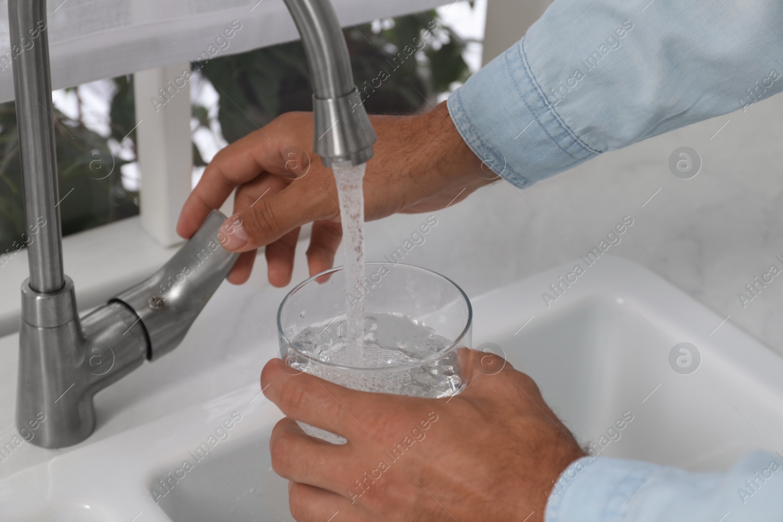 Photo of Man filling glass with water from tap at home, closeup