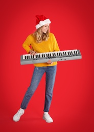 Photo of Young woman in Santa hat playing synthesizer on red background. Christmas music