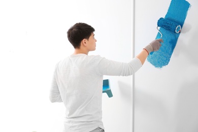 Male decorator painting wall with roller indoors