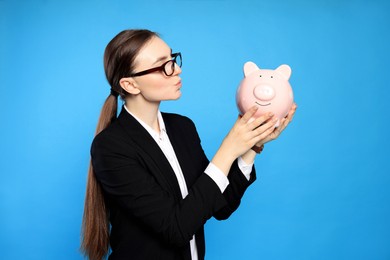 Photo of Young businesswoman with piggy bank on light blue background