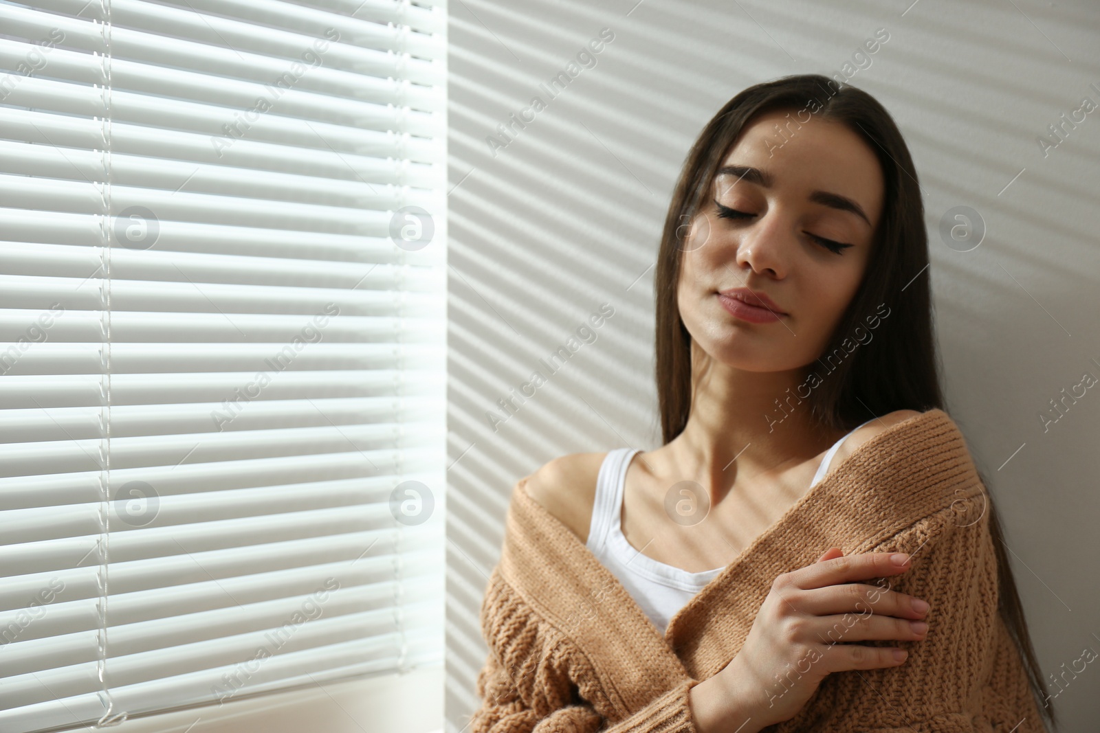 Photo of Young woman near window with Venetian blinds. Space for text