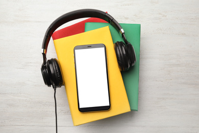 Books with modern headphones and smartphone on white wooden background, top view. Space for design