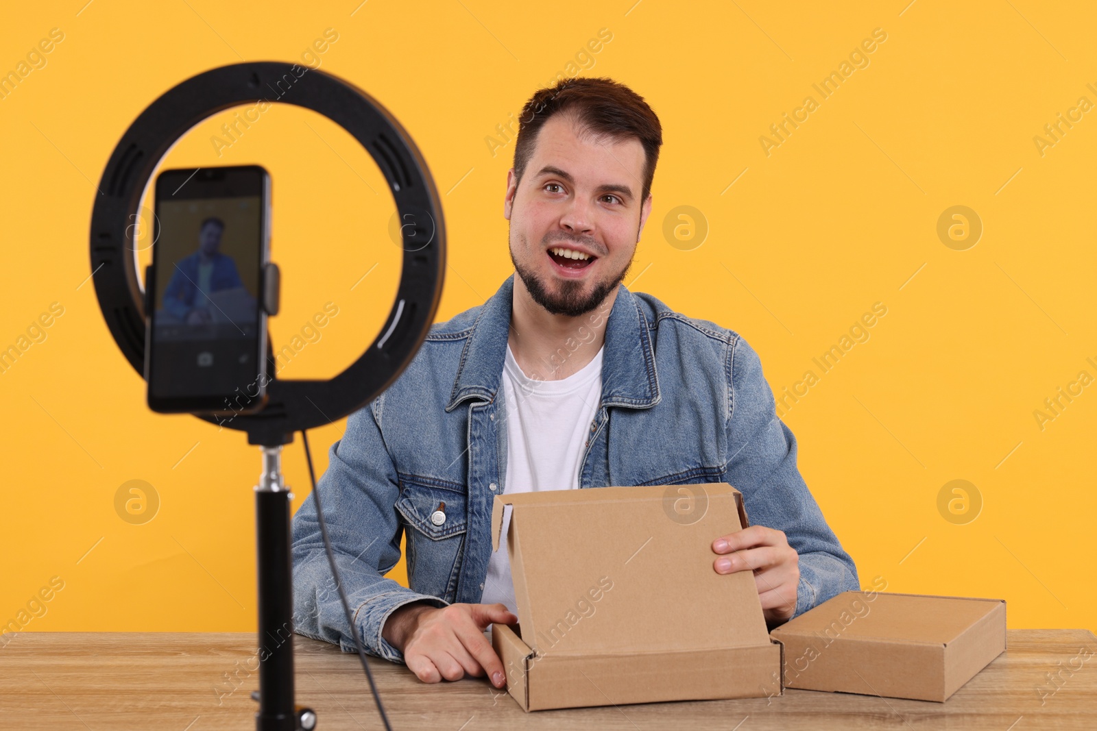 Photo of Happy fashion blogger with parcels recording video at table against orange background