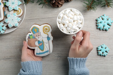 Woman with tasty gingerbread cookie and cup of hot drink at wooden table, top view. St. Nicholas Day celebration