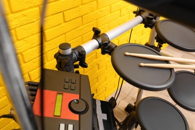 Photo of Modern electronic drum kit near yellow brick wall indoors. Musical instrument
