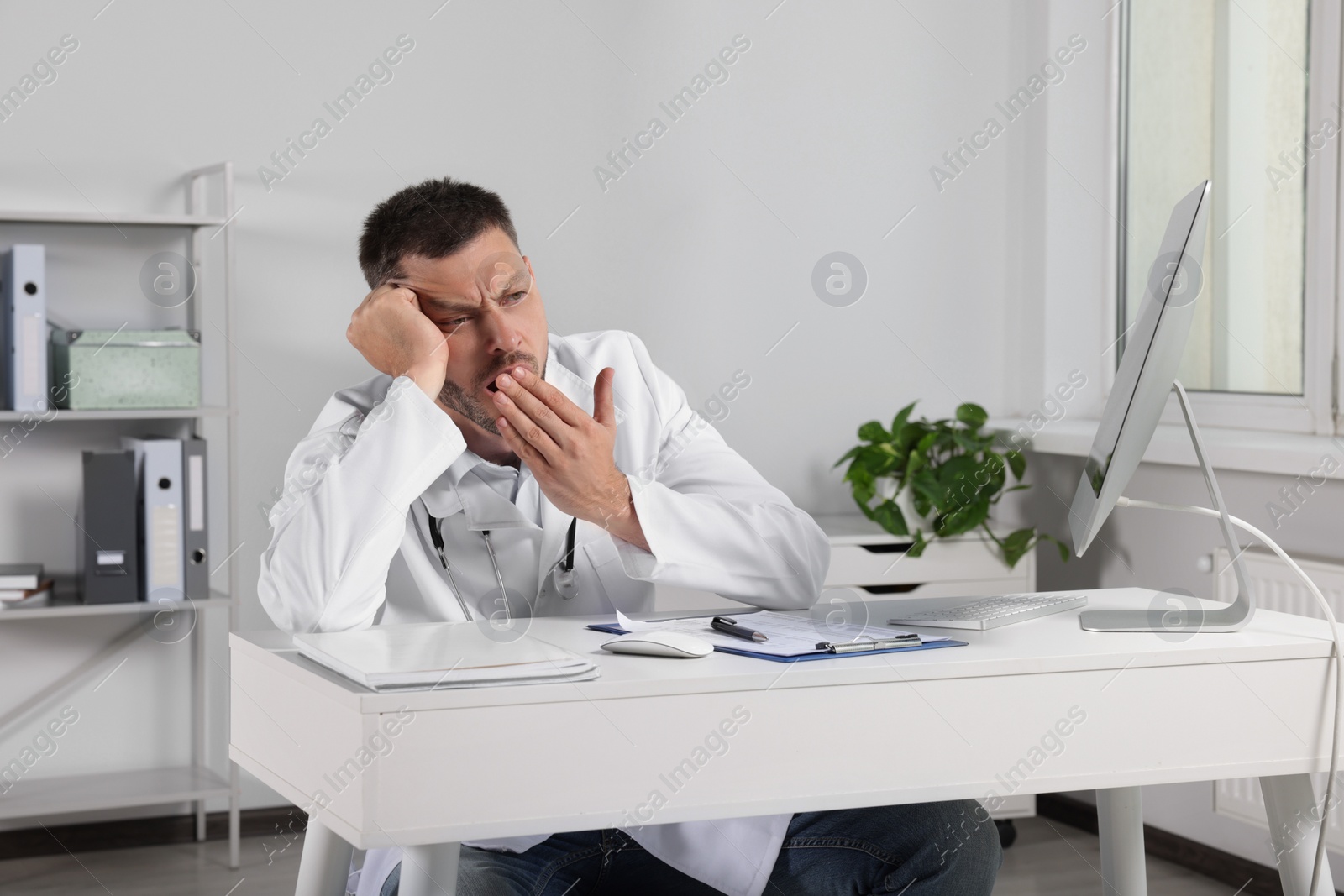 Photo of Exhausted doctor yawning at workplace in hospital