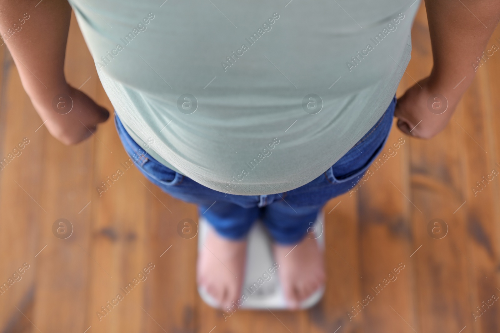 Photo of Overweight boy standing on floor scales indoors, above view