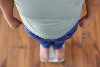 Overweight boy standing on floor scales indoors, above view