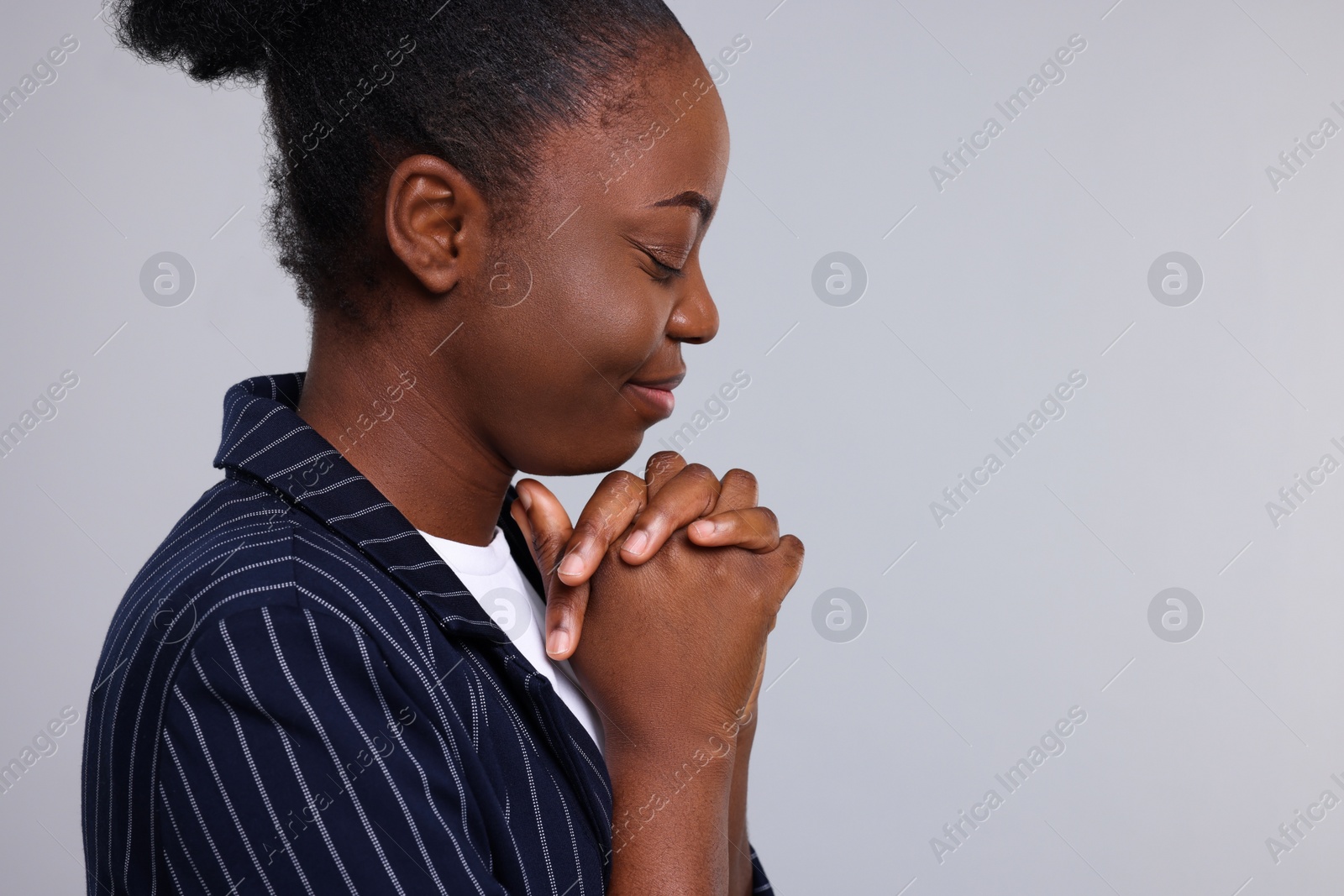 Photo of Woman with clasped hands praying to God on light grey background. Space for text