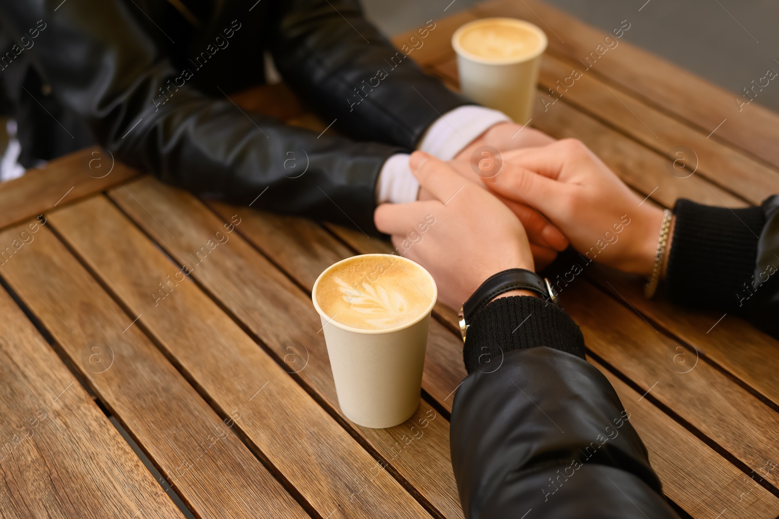 Photo of Lovely couple with coffee holding hands together at wooden table outdoors, closeup. Romantic date