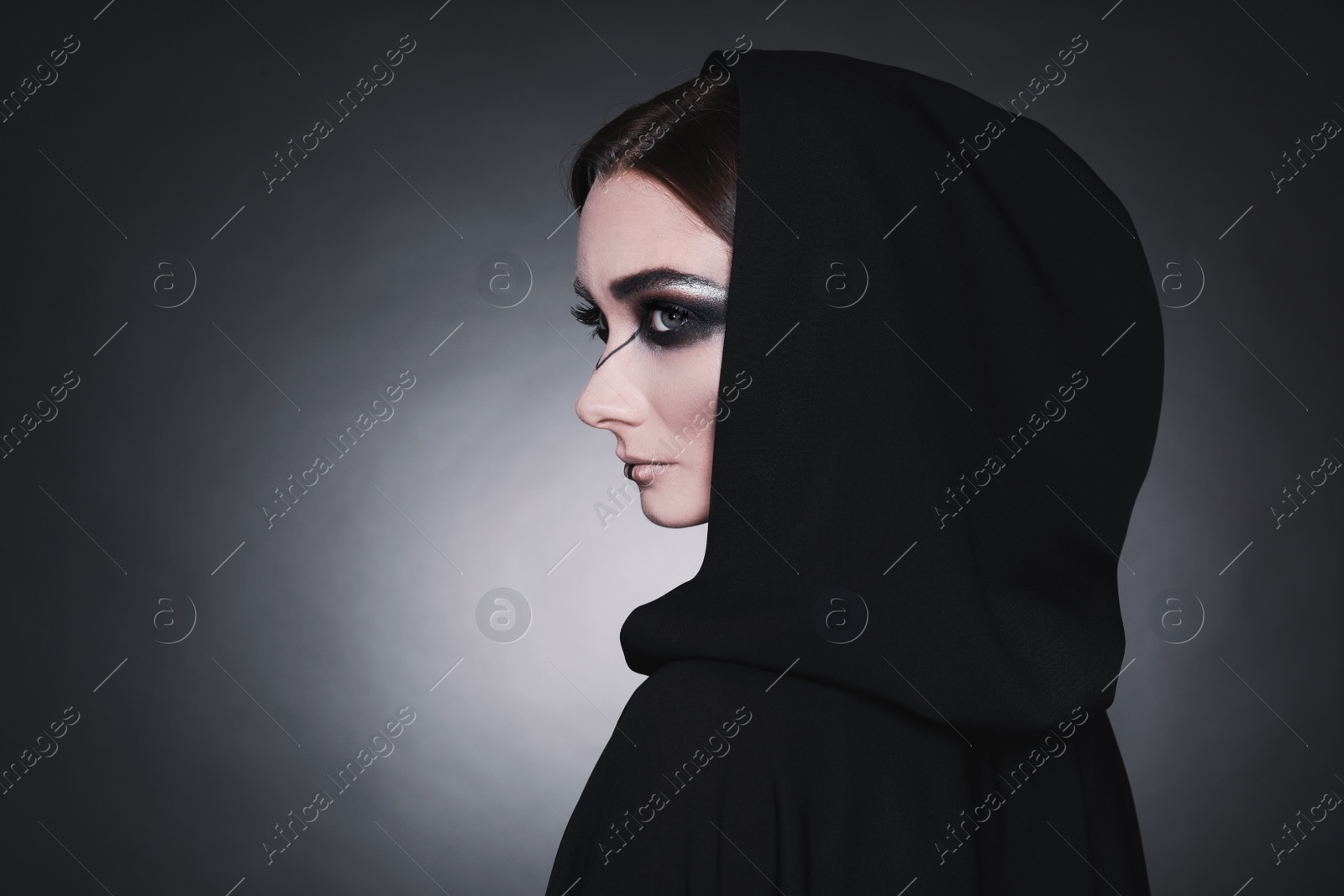Photo of Mysterious witch in mantle with hood on dark background. Space for text