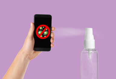 Image of Sanitizing mobile devices during coronavirus outbreak. Antiseptic spray and man with smartphone on lilac background, closeup