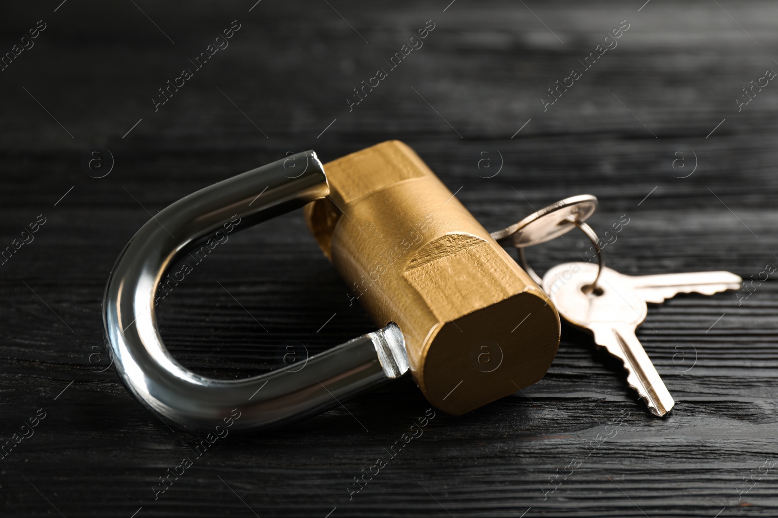 Photo of Modern padlock with keys on black wooden table, closeup
