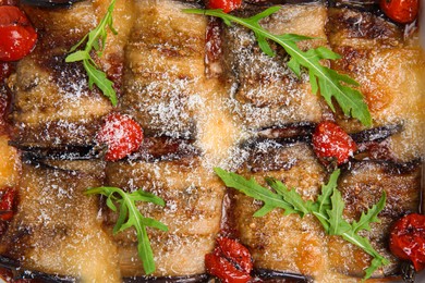 Tasty eggplant rolls with tomatoes, cheese and arugula as background, top view