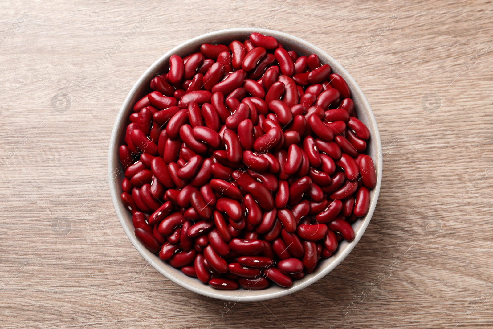 Photo of Raw red kidney beans in bowl on wooden table, top view