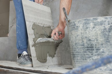 Worker applying cement on wall tile for installation indoors, closeup