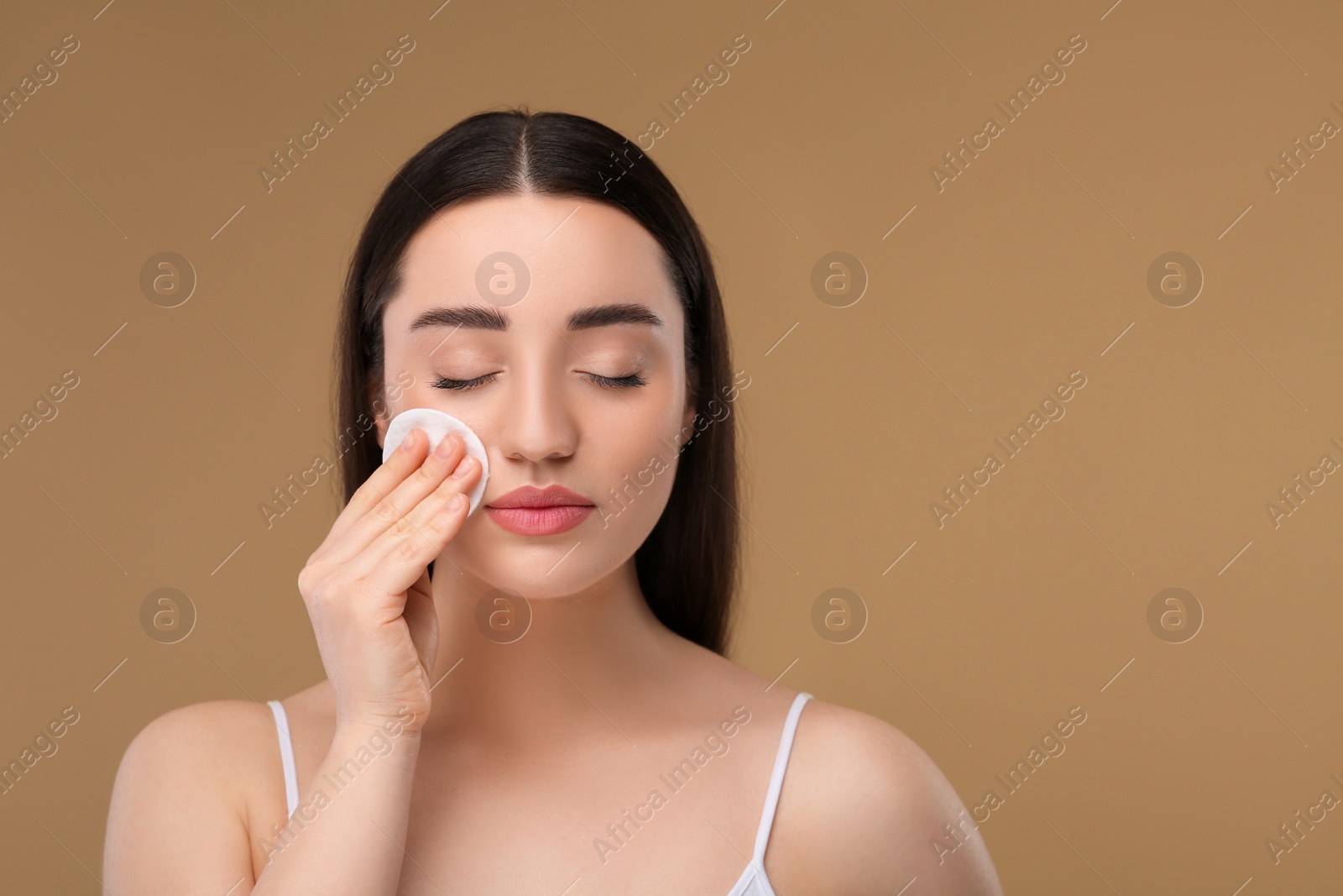 Photo of Beautiful woman removing makeup with cotton pad on beige background, space for text