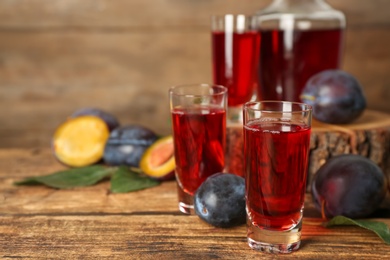 Photo of Delicious plum liquor and ripe fruits on wooden table. Homemade strong alcoholic beverage
