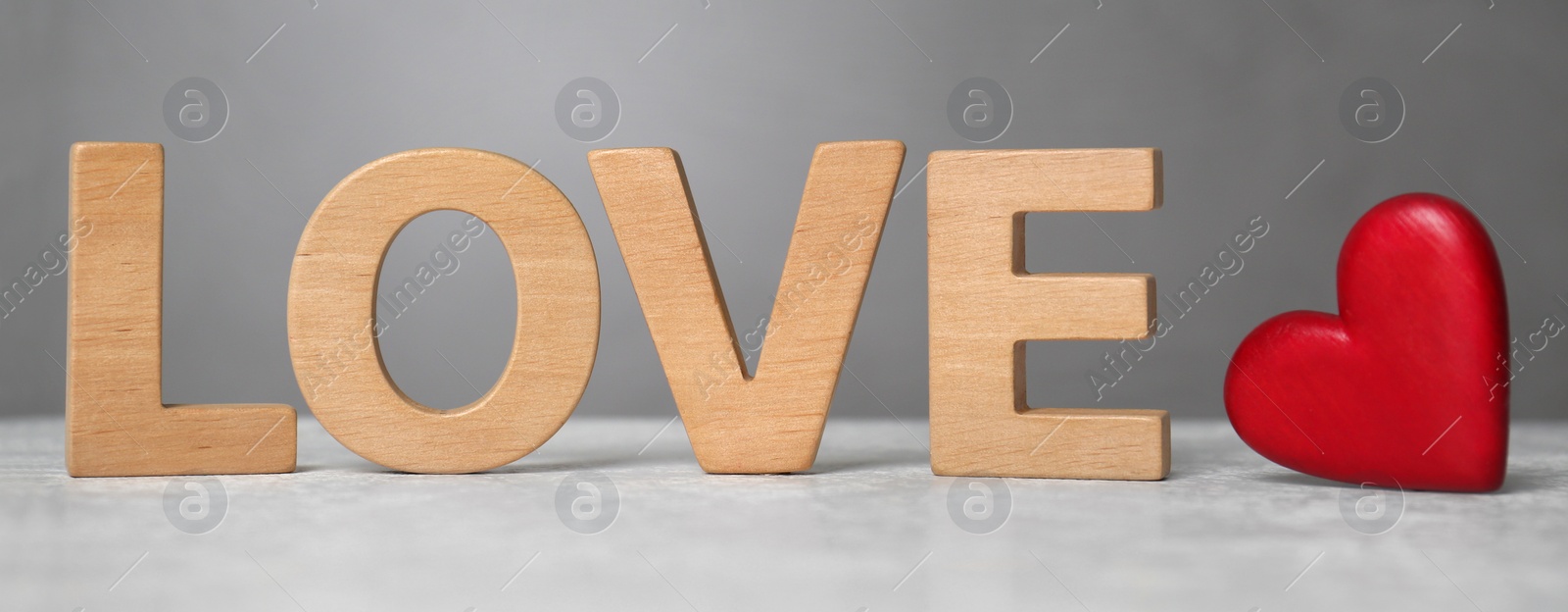 Photo of Word Love made of wooden letters near red decorative heart on light table