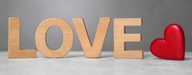 Photo of Word Love made of wooden letters near red decorative heart on light table