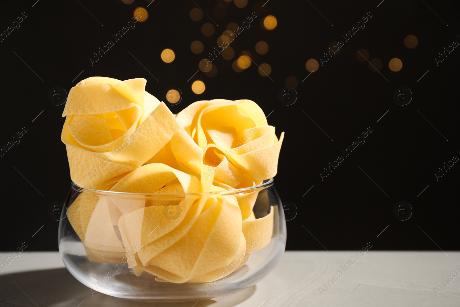 Photo of Uncooked pappardelle pasta on grey table against blurred lights