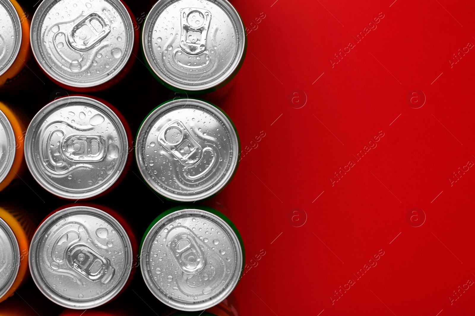 Photo of Energy drinks in wet cans on red background, top view. Space for text