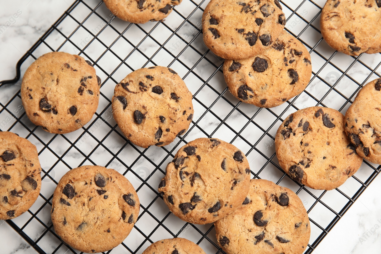 Photo of Cooling rack with chocolate chip cookies on marble background, top view