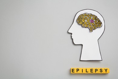 Photo of Human head cutout, brain and yellow cubes with word Epilepsy on light grey background, flat lay. Space for text
