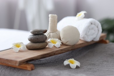 Stacked spa stones, flowers, herbal bags and towel on massage table indoors, closeup