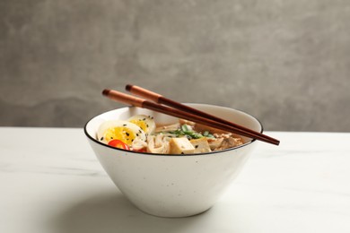 Bowl of delicious ramen and chopsticks on white marble table. Noodle soup