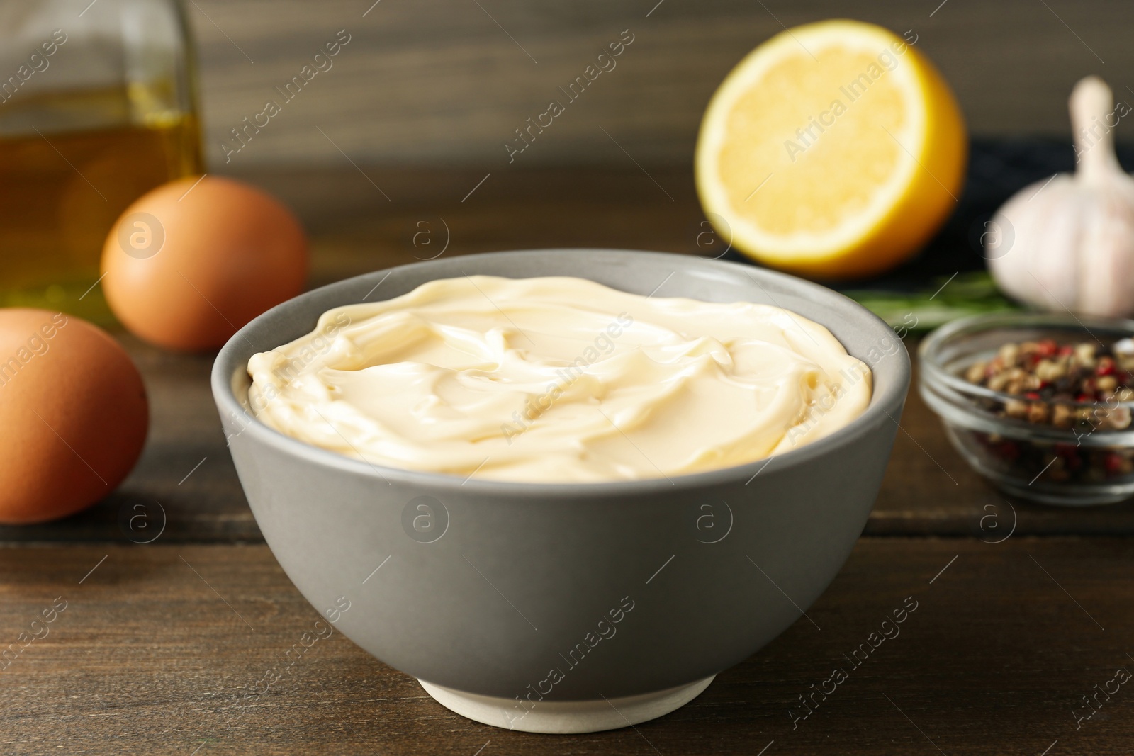 Photo of Bowl with fresh mayonnaise and ingredients on wooden table, closeup