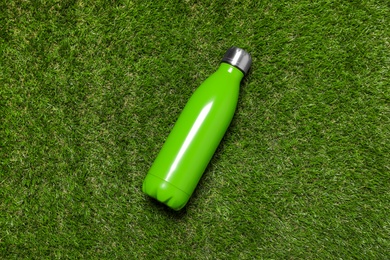 Photo of Modern green thermos bottle on grass, top view