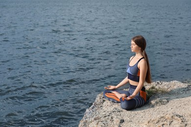 Photo of Teenage girl meditating on cliff near river. Space for text