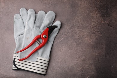 Pair of gardening gloves and secateurs on brown textured table, top view. Space for text