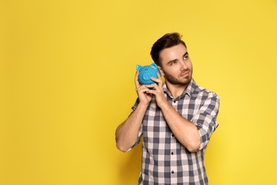 Young man with piggy bank on color background. Space for text