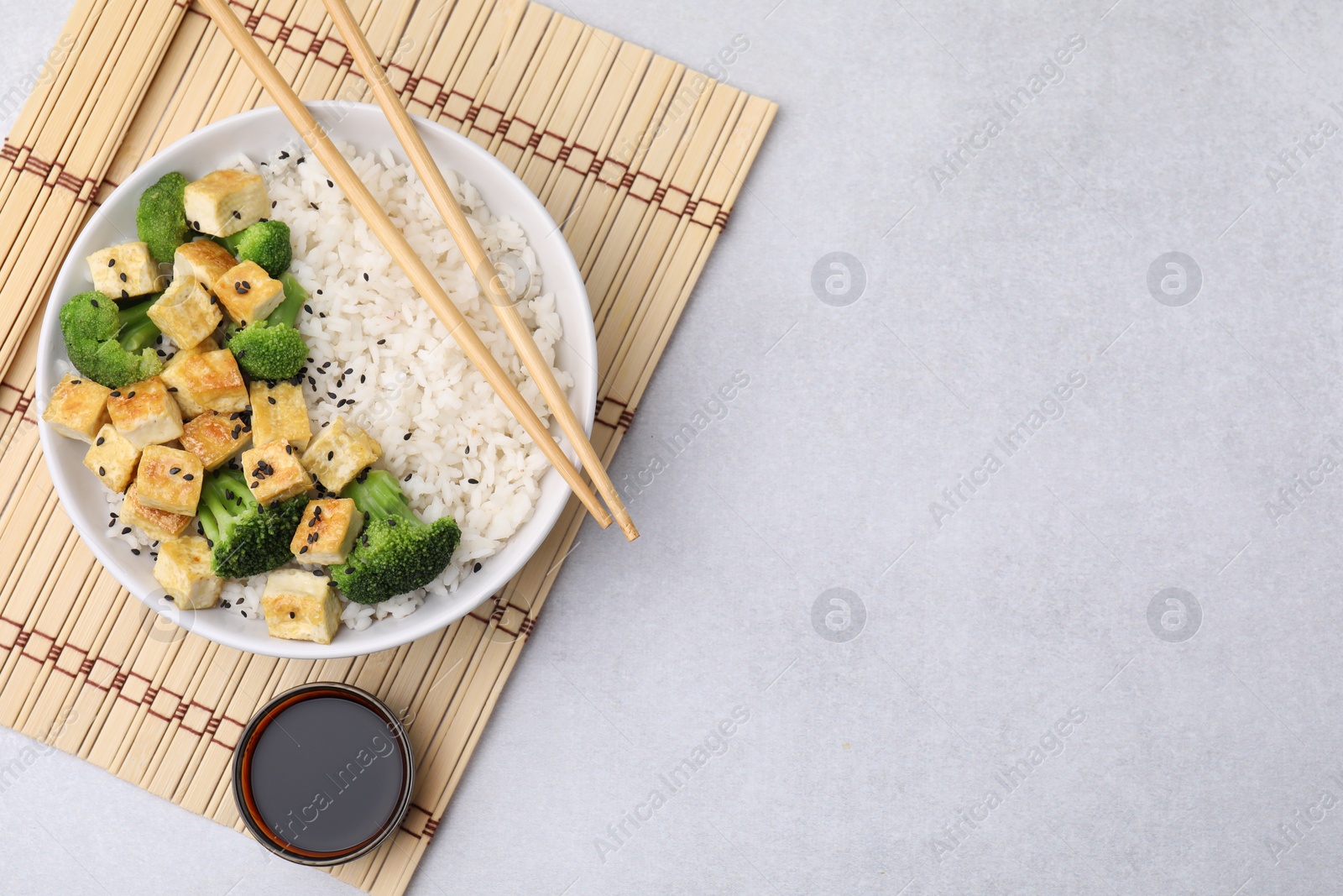 Photo of Bowl of rice with fried tofu and broccoli on white table, top view. Space for text