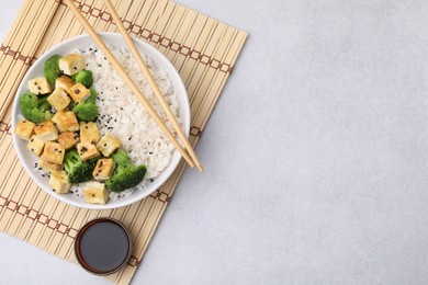 Bowl of rice with fried tofu and broccoli on white table, top view. Space for text