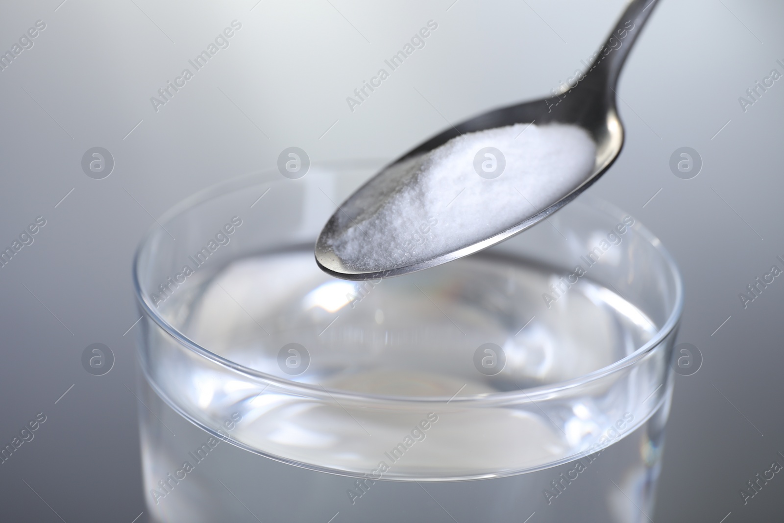 Photo of Adding baking soda into glass of water on light grey background, closeup