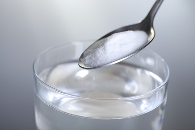 Adding baking soda into glass of water on light grey background, closeup