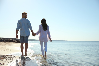 Young couple walking on beach near sea, back view. Honeymoon trip