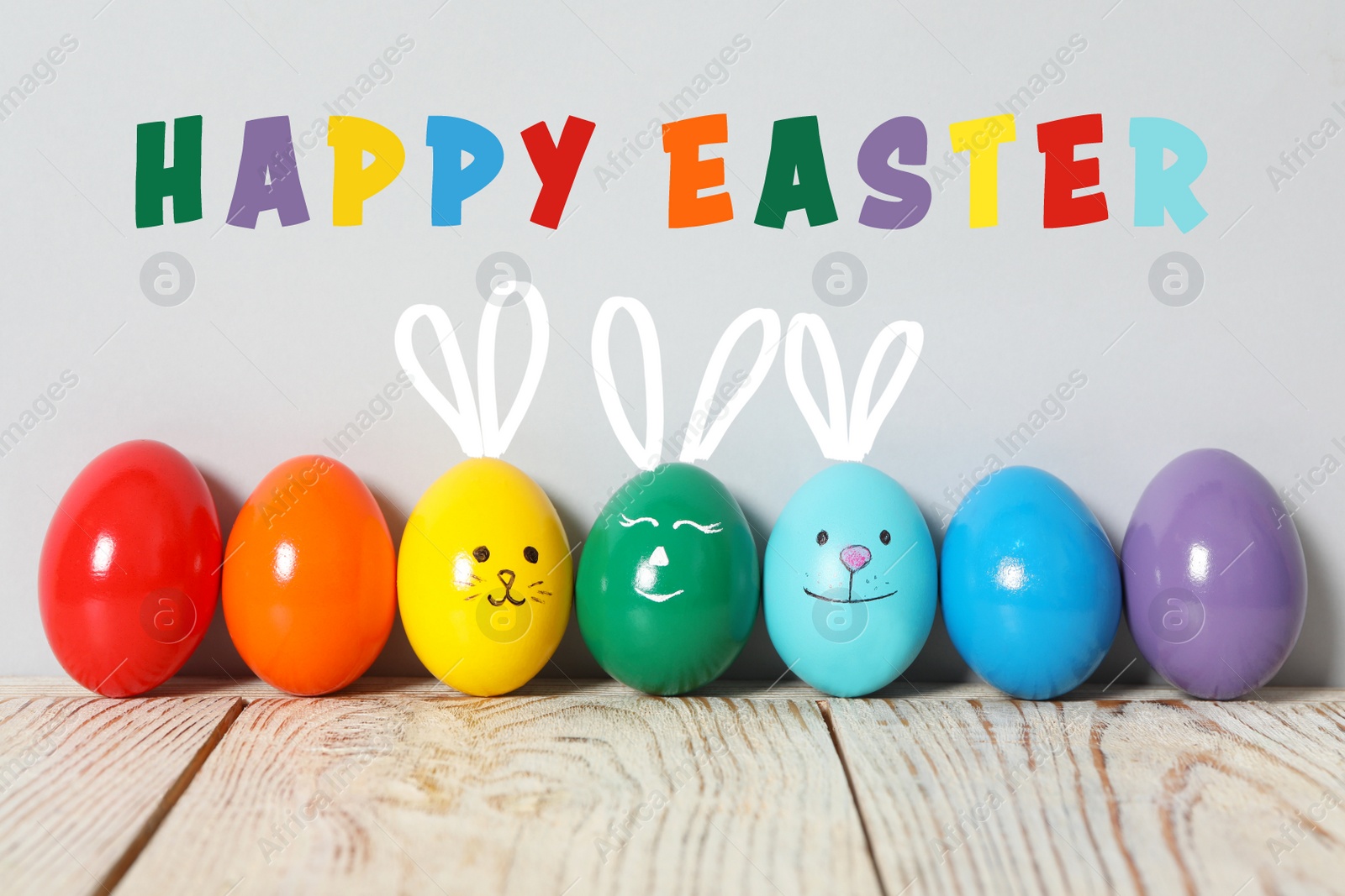 Image of Several eggs with drawn faces and ears as Easter bunnies among others on white wooden table against light grey background