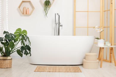 Photo of Stylish bathroom interior with bath tub, houseplants and bamboo mat