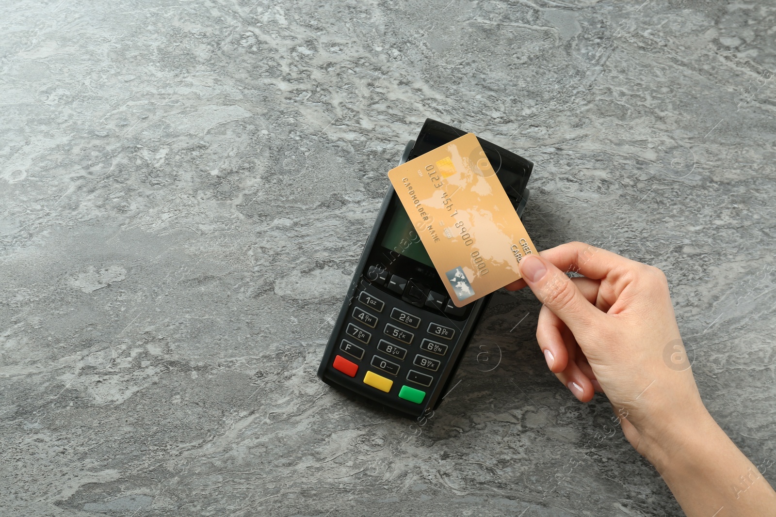 Photo of Woman with credit card using modern payment terminal at grey table, top view