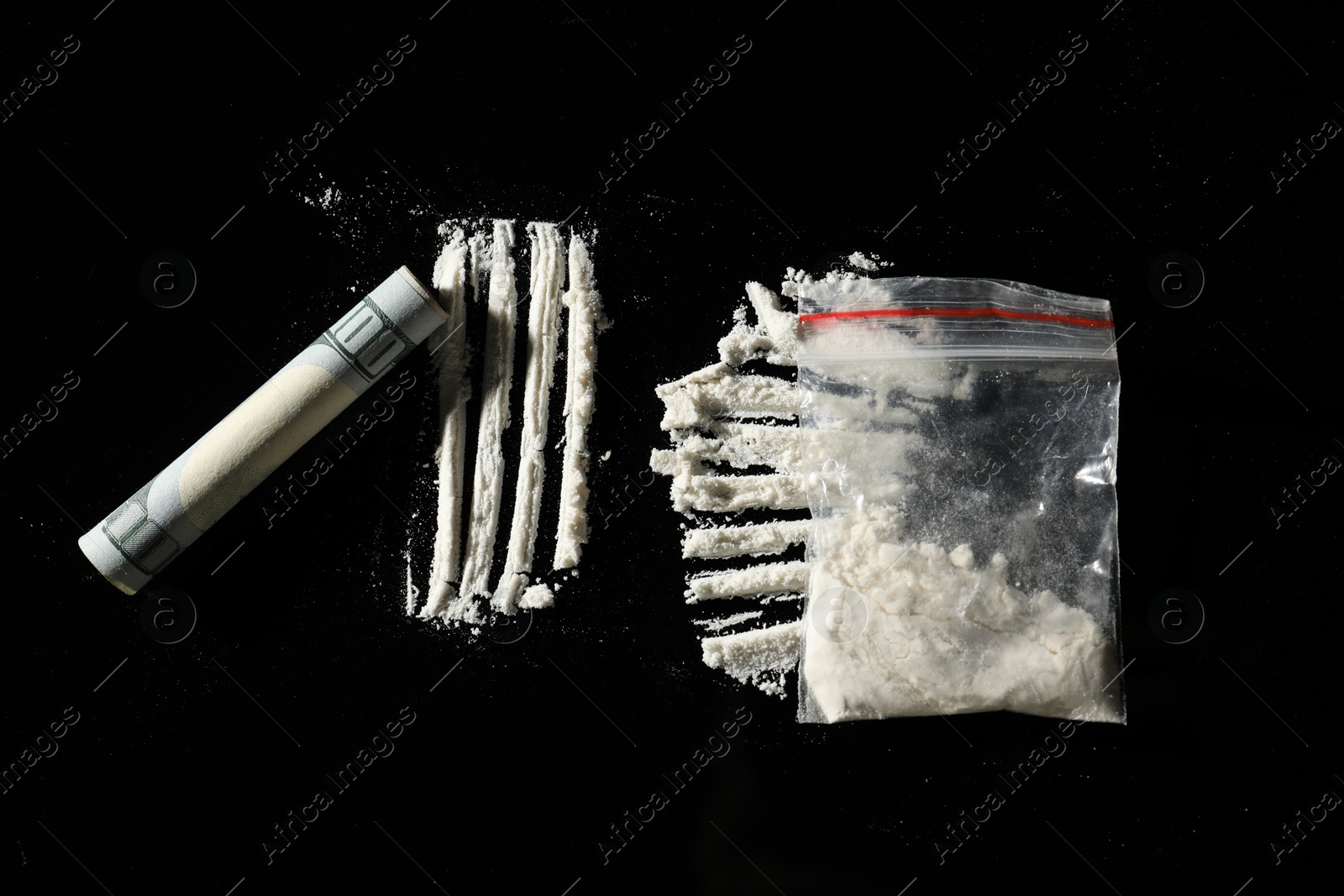 Photo of Drug addiction. Plastic bag with cocaine and rolled dollar banknote on black background, flat lay